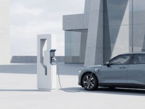 Moderne elektrische auto wordt opgeladen bij wit laadstation met blauwe accentverlichting en minimalistische architectuur