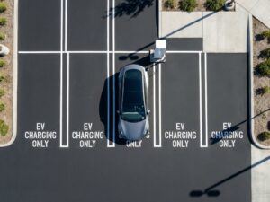 Elektrische auto verbonden met laadpaal in moderne parkeerplaats met witte markeringen, luchtfoto in fel daglicht