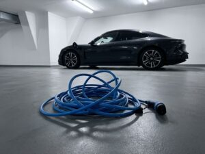 Losgekoppelde blauwe EV-laadkabel op garagevloer met elektrische auto op achtergrond met open laadpoort