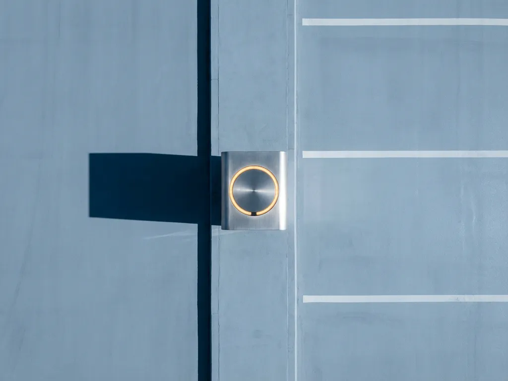 Elektrische laadpaal in lege moderne kantoorparkeerplaats met geometrische schaduw op beton, warme amber indicator