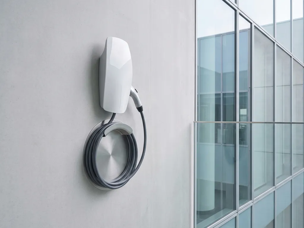 Wit elektrisch auto-oplaadstation gemonteerd op betonnen muur naast modern glazen kantoorgebouw