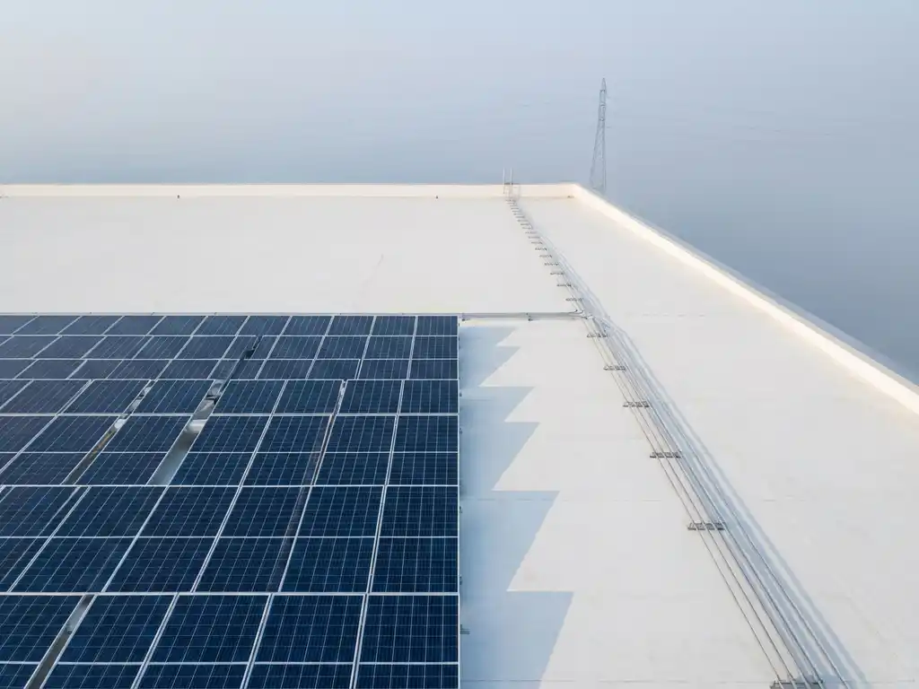 Zonnepanelen werpen geometrische schaduwen op wit dak met elektrische kabels naar stroomnet toren in de verte